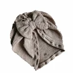 Hier een schattig zandkleurige turban mutsje gemaakt van geweven stof met kabelmotief. Het mutsje heeft aan de voorkant een leuke strik. Door de stof krijgt dit mutsje een speelse en mooie uitstraling.