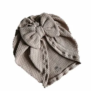 Hier een schattig zandkleurige turban mutsje gemaakt van geweven stof met kabelmotief. Het mutsje heeft aan de voorkant een leuke strik. Door de stof krijgt dit mutsje een speelse en mooie uitstraling.