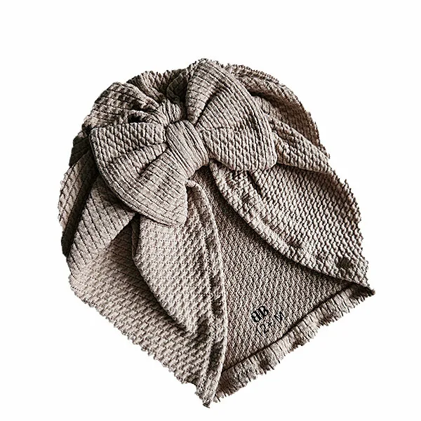 Hier een schattig zandkleurige turban mutsje gemaakt van geweven stof met kabelmotief. Het mutsje heeft aan de voorkant een leuke strik. Door de stof krijgt dit mutsje een speelse en mooie uitstraling.