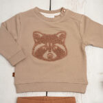 Deze stoere sweater in de kleur taupe komt uit de Racoon Club collectie van Frogs and Dogs. De sweater is gemaakt van zacht katoen. Op de voorzijde is het hoofdje van een wasbeer geborduurd met wollige garen waardoor het er echt op ligt. Aan de binnenzijde is vlies gebruik waardoor de huid van je kleintje beschermd wordt.