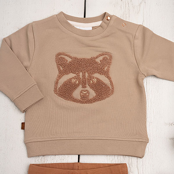 Deze stoere sweater in de kleur taupe komt uit de Racoon Club collectie van Frogs and Dogs. De sweater is gemaakt van zacht katoen. Op de voorzijde is het hoofdje van een wasbeer geborduurd met wollige garen waardoor het er echt op ligt. Aan de binnenzijde is vlies gebruik waardoor de huid van je kleintje beschermd wordt.