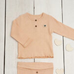 Dit leuke zalmkleurige shirtje met lange mouwen komt uit de Amour collectie van Frogs and Dogs. Het shirtje is gemaakt van ribstof en is effen van kleur. De sluiting van dit shirtje zit op de voorzijden en heeft 2 knoopjes en het boordje van de hals is afgezet met een kanten randje. De mouwen hebben een omgeslagen boord afgezet met een kanten randje. De onderkant van het shirtje is gestikt waardoor het een leuke schulprand heeft.