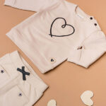 Beige babysweater met donkerblauw geborduurd hartje, gebreide boorden en knoopsluiting op de schouder uit de Amour-collectie van Frogs and Dogs