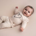 Beige babysweater met donkerblauw geborduurd hartje, gebreide boorden en knoopsluiting op de schouder uit de Amour-collectie van Frogs and Dogs