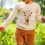 Deze unieke romper/shirt met lange mouw komt uit de collectie van MijsXMerlijn. Het is eigenlijk een mouwloze romper met daaraan vast een shirt met lange mouwen. De combinatie is off-white van kleur met een print van een giraffe hoofs. Er zit een drukker sluiting op de linkerschouder en tussen de beentjes. 