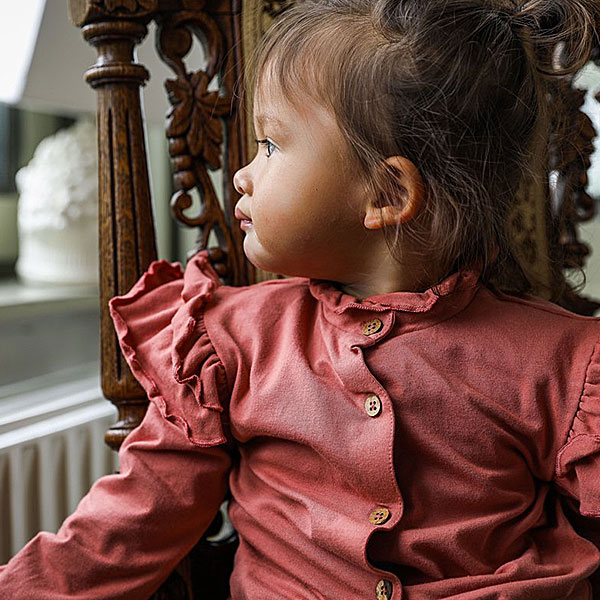 Dit prachtige roze ruffle baby blouse met unieke houten knoopjes heeft ruffles op de kraag en schouders. En is gemaakt van een zachte elastische kwaliteit wat comfort en warmte biedt voor je kleintje. De boord van de mouwtjes zijn afgewerkt met elastiek waardoor het aankleden nog makkelijker is.