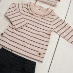 Dit leuke beige shirtje met lange mouwen komt uit de Amour collectie van Frogs and Dogs. Het shirtje is gemaakt van zachte katoen en heeft een fijne strepenprint de kleur zwart. De sluiting van dit shirtje zit op de voorzijden en heeft 2 knoopjes en het boordje van de hals is afgezet met een kanten randje. De mouwen hebben een omgeslagen boord afgezet met een kanten randje. De onderkant van het shirtje is gezoomd.