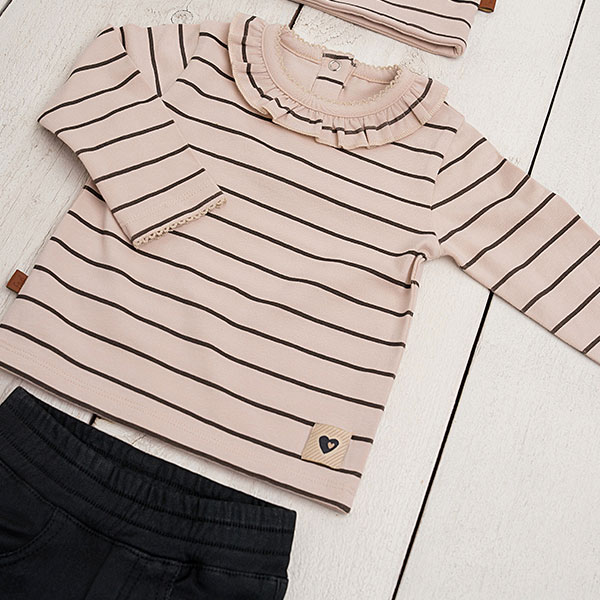 Dit leuke beige shirtje met lange mouwen komt uit de Amour collectie van Frogs and Dogs. Het shirtje is gemaakt van zachte katoen en heeft een fijne strepenprint de kleur zwart. De sluiting van dit shirtje zit op de voorzijden en heeft 2 knoopjes en het boordje van de hals is afgezet met een kanten randje. De mouwen hebben een omgeslagen boord afgezet met een kanten randje. De onderkant van het shirtje is gezoomd.