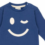 Deze stoere blauwe baby sweater met een grote, geprinte knipogende smile komt uit de collectie Happy With You van Frogs and Dogs. De print staat op de voorzijde en geeft een speelse en vrolijke uitstraling.