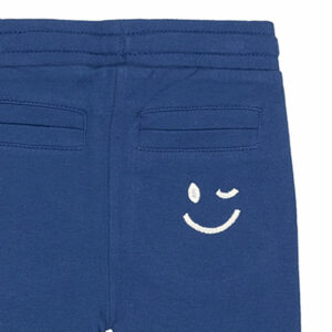 Schattige donkerblauwe joggingbroek uit de Happy with You-collectie van Frogs and Dogs. Het broekje is gemaakt van heerlijk zacht katoen en zit supercomfortabel. De broek heeft twee steekzakjes aan de voorkant en twee kontzakjes aan de achterkant. Op een van de achterzakjes zit een geborduurde, beige smiley die ondeugend knipoogt — een speels detail! De pijpjes zijn afgewerkt met een ingenaaide elastiek, waardoor ze mooi aansluiten. Dankzij de elastische tailleband met koord blijft de broek goed op zijn plek, hoe actief je kleintje ook is.