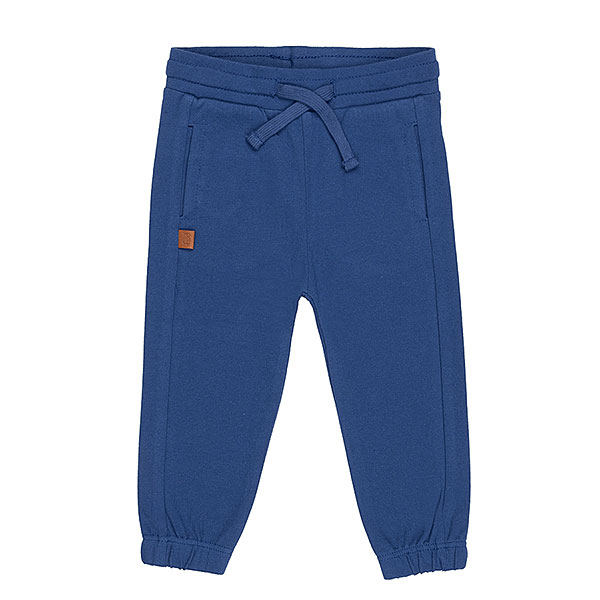 Schattige donkerblauwe joggingbroek uit de Happy with You-collectie van Frogs and Dogs. Het broekje is gemaakt van heerlijk zacht katoen en zit supercomfortabel. De broek heeft twee steekzakjes aan de voorkant en twee kontzakjes aan de achterkant. Op een van de achterzakjes zit een geborduurde, beige smiley die ondeugend knipoogt — een speels detail! De pijpjes zijn afgewerkt met een ingenaaide elastiek, waardoor ze mooi aansluiten. Dankzij de elastische tailleband met koord blijft de broek goed op zijn plek, hoe actief je kleintje ook is.