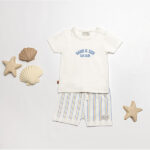 Baby t-shirtje gebroken wit met blauwe tekst Sand & Sun – Sea Club van Frogs and Dogs. Zacht katoen, ideaal voor warme zomerdagen.