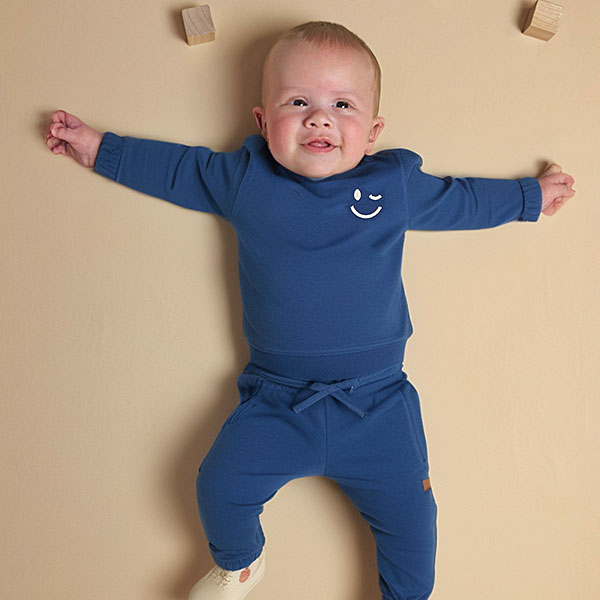 Blauwe baby sweater van Frogs and Dogs met subtiele smiley op de borst. Zacht, comfortabel en ideaal voor frisse zomerdagen.