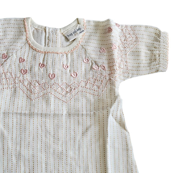 Deze prachtige Gold Glitter blouse uit de All Collection Summer van Frogs and Dogs straalt pure elegantie uit. Het blouseje is gemaakt van crèmekleurige stof met subtiele, gestippelde streepjes en een schitterende goudglitter. Op borsthoogte bevindt zich een gestikte rand met roze garen, net erboven zijn schattige hartjes geborduurd.