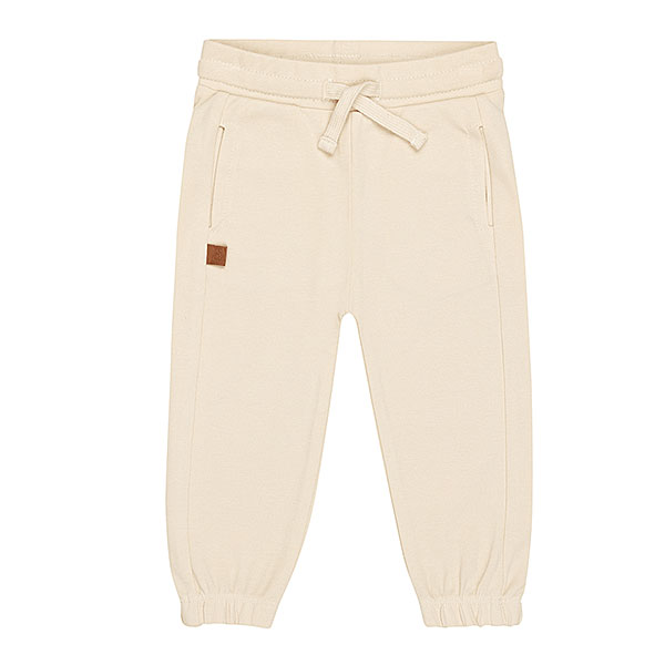 Schattige beige joggingbroek uit de Happy with You collectie van Frogs and Dogs. Het broekje is gemaakt van heerlijk zacht katoen en zit supercomfortabel. De broek heeft twee steekzakjes aan de voorkant en twee nep kontzakjes aan de achterkant. Op een van de achterzakjes zit een geborduurde, blauwe smiley die ondeugend knipoogt — een speels detail!