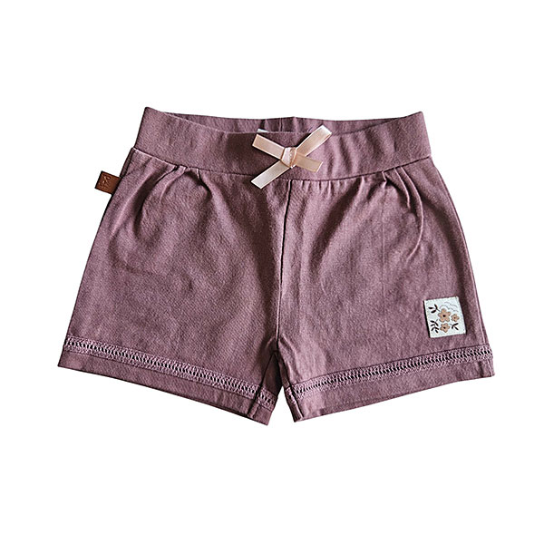 Dit schattige korte broekje, ook wel short, in de kleur Burlwoord komt uit de Summer Flowers-collectie van Frogs and Dogs. Het korte broekje heeft een zachte, effen tint en is gemaakt van comfortabel materiaal, perfect voor warme zomerdagen. De elastische tailleband biedt een fijne pasvorm en is afgewerkt met een roze strikje. Boven de zoom van het pijpje zit een leuk kanten randje verwerkt. Een perfecte mix van stijl en comfort voor een zomerse look!