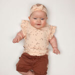 Dit lieve t-shirtje in de zachte tint Pale Dogwood komt uit de Love Garden-collectie van Frogs and Dogs. Het t-shirtje heeft een charmante all-over print van kleine bloemetjes in de warme kleur Burlwood (bruin). De speelse ruffle-rand op de schouders geeft het t-shirtje een extra vrolijke touch. Aan de achterkant zorgt een handige sluiting met drie drukknoopjes voor gemakkelijk aan- en uittrekken. De mouwtjes en onderkant zijn netjes omgezoomd voor een mooie afwerking.