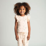 Dit lieve t-shirtje in de zachte tint Pale Dogwood komt uit de Love Garden-collectie van Frogs and Dogs. Het t-shirtje heeft een charmante all-over print van kleine bloemetjes in de warme kleur Burlwood (bruin). De speelse ruffle-rand op de schouders geeft het t-shirtje een extra vrolijke touch. Aan de achterkant zorgt een handige sluiting met drie drukknoopjes voor gemakkelijk aan- en uittrekken. De mouwtjes en onderkant zijn netjes omgezoomd voor een mooie afwerking.