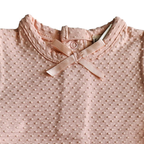 Dit lieve Bubble t-shirtje met korte mouwen in een zachte zalmroze kleur komt uit de Summer Flowers collectie van Frogs and Dogs. Het shirtje is gemaakt van een fijne, luchtige stof met een speels bubbeltjespatroon, wat zorgt voor een subtiele textuur en een extra schattige uitstraling. Een sierlijk strikje op de halsrand aan de voorzijde voegt een charmante en verfijnde touch toe. De gezoomde randen van de mouwtjes zijn afgewerkt met een elegant kanten randje, wat het geheel een romantisch en lieflijk karakter geeft. Aan de achterzijde is een handige drukknoopsluiting aangebracht, zodat het t-shirtje gemakkelijk aan- en uitgetrokken kan worden.