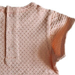 Dit lieve Bubble t-shirtje met korte mouwen in een zachte zalmroze kleur komt uit de Summer Flowers collectie van Frogs and Dogs. Het shirtje is gemaakt van een fijne, luchtige stof met een speels bubbeltjespatroon, wat zorgt voor een subtiele textuur en een extra schattige uitstraling. Een sierlijk strikje op de halsrand aan de voorzijde voegt een charmante en verfijnde touch toe. De gezoomde randen van de mouwtjes zijn afgewerkt met een elegant kanten randje, wat het geheel een romantisch en lieflijk karakter geeft. Aan de achterzijde is een handige drukknoopsluiting aangebracht, zodat het t-shirtje gemakkelijk aan- en uitgetrokken kan worden.