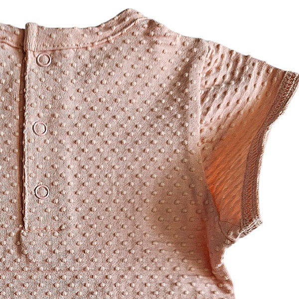 Dit lieve Bubble t-shirtje met korte mouwen in een zachte zalmroze kleur komt uit de Summer Flowers collectie van Frogs and Dogs. Het shirtje is gemaakt van een fijne, luchtige stof met een speels bubbeltjespatroon, wat zorgt voor een subtiele textuur en een extra schattige uitstraling. Een sierlijk strikje op de halsrand aan de voorzijde voegt een charmante en verfijnde touch toe. De gezoomde randen van de mouwtjes zijn afgewerkt met een elegant kanten randje, wat het geheel een romantisch en lieflijk karakter geeft. Aan de achterzijde is een handige drukknoopsluiting aangebracht, zodat het t-shirtje gemakkelijk aan- en uitgetrokken kan worden.