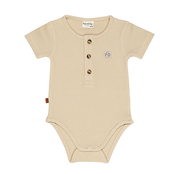 Dit zandkleurige rompertje met wafelstructuur komt uit de All Collection van Frogs and Dogs en is ideaal voor de zomer. Het is gemaakt van een zachte stof en heeft korte mouwen. De voorzijde is voorzien van een sluiting met drie knoopjes, en tussen de beentjes zit een drukknoopsluiting. Het rompertje kan los gedragen worden bij warm weer of gecombineerd worden met een vestje op koelere dagen.