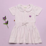 Dit mooie jurkje in de kleur Lavender Fog komt uit de Beautiful Hearts collectie van Frogs and Dogs. Het jurkje heeft een schattig kraagje en een drukknoopsluiting aan de voorzijde. Op het borstzakje prijkt een paars geborduurd hartje. De mouwtjes zijn licht gepoft en het rokje heeft een speelse, gerimpelde zoom. In de taille bevindt zich een elastische rand met een strikje, wat de jurk een extra charmante uitstraling geeft. Het rokje is voorzien van 2 steekzakjes.