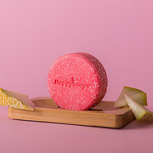 Happysoaps You’re One in a Melon Shampoo Bar in roze kleur met verpakking op roze achtergrond.